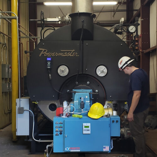 Man with white hardhat standing next to Power Matt steam boiler installed in a corn syrup transfer station.